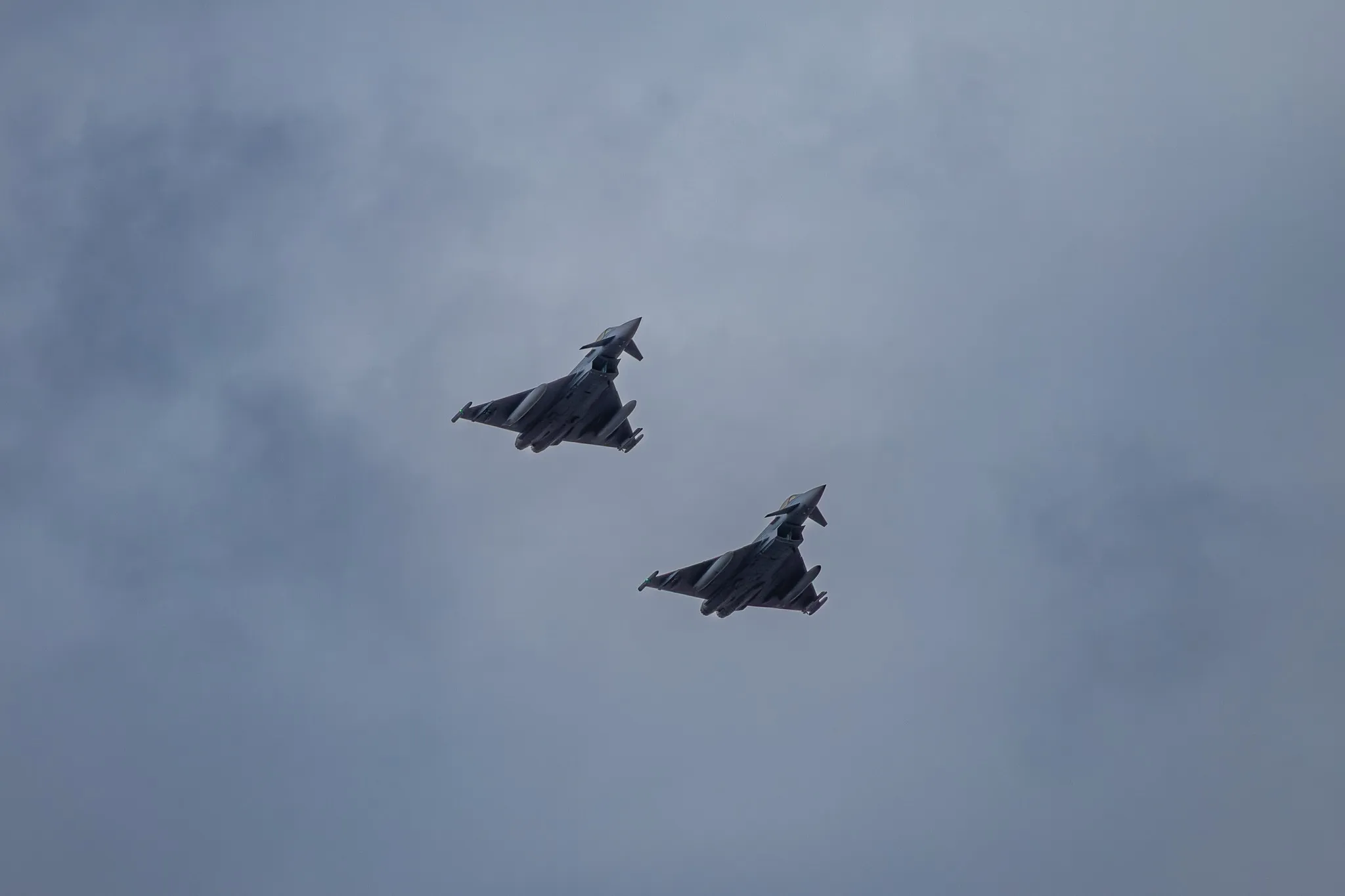 Zwei Eurofighter Typhoon fliegen in Formation, Deltaflügel und Canards von unten sichtbar vor bewölktem Himmel.