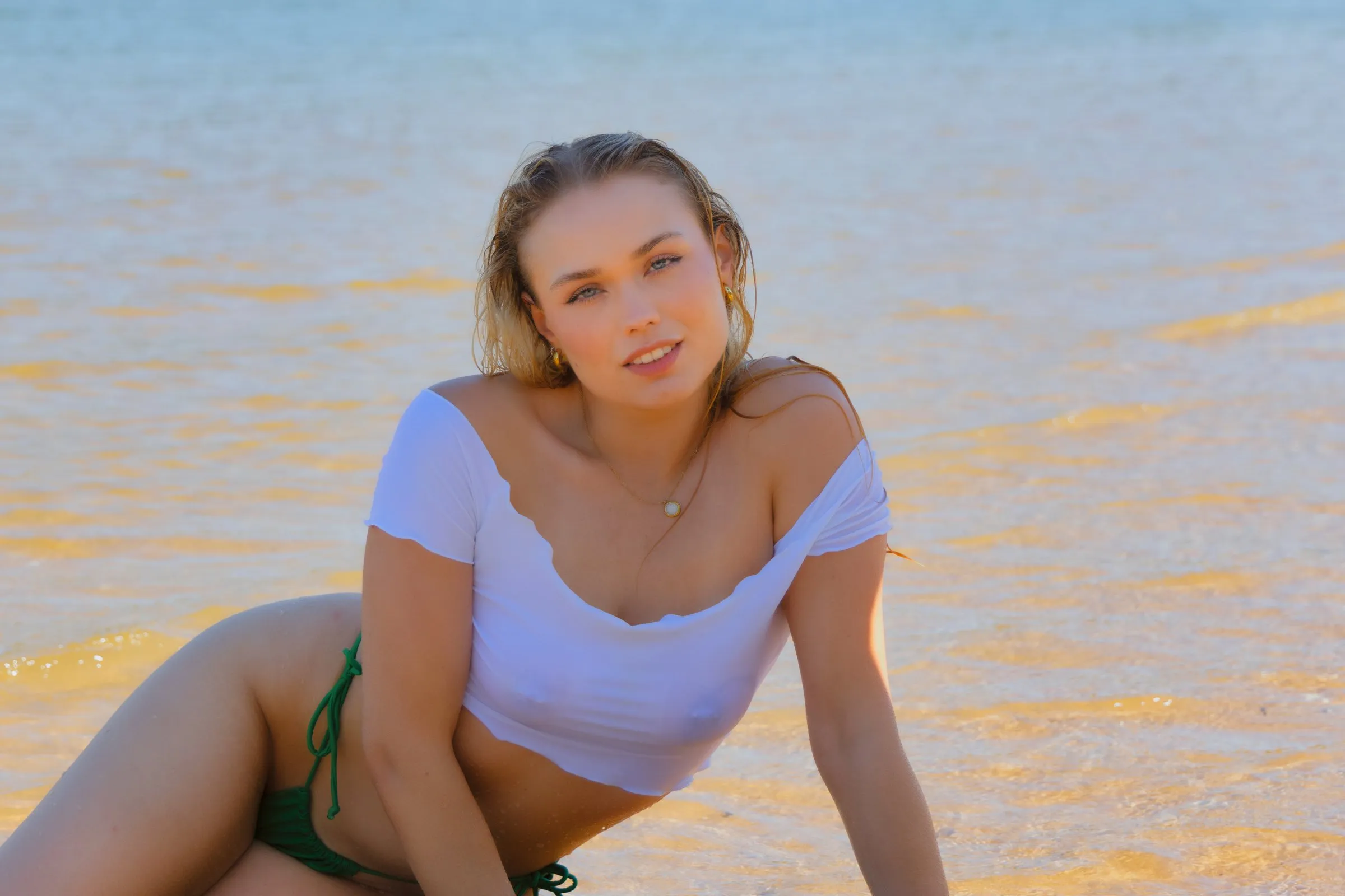 Junge Frau lehnt sich am Wasser nach vorne, Sand und Wasser prägen den Bildhintergrund.
