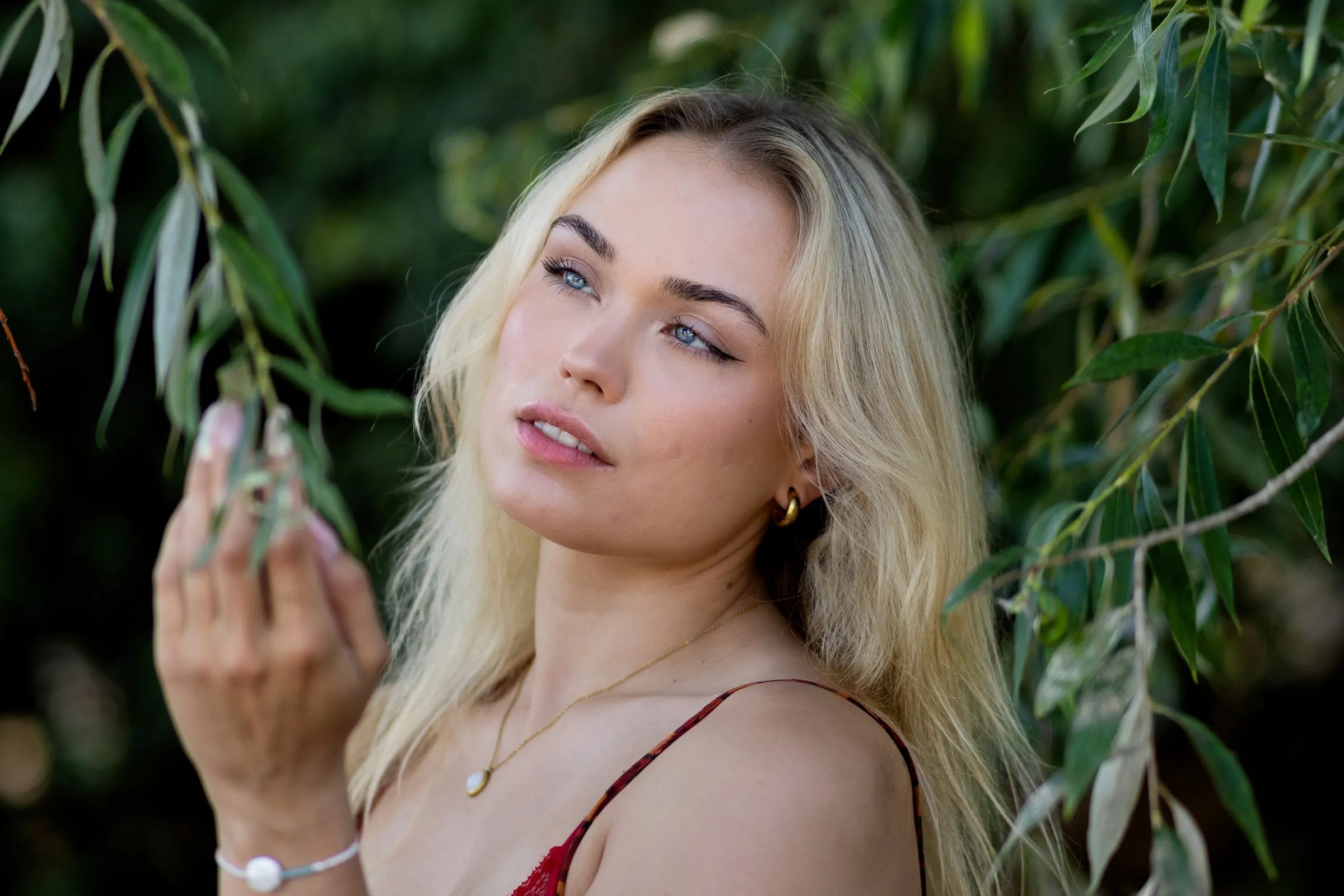 Junge Frau hält Blätter in der Hand und blickt nachdenklich zur Seite, im Hintergrund unscharfes Grün.