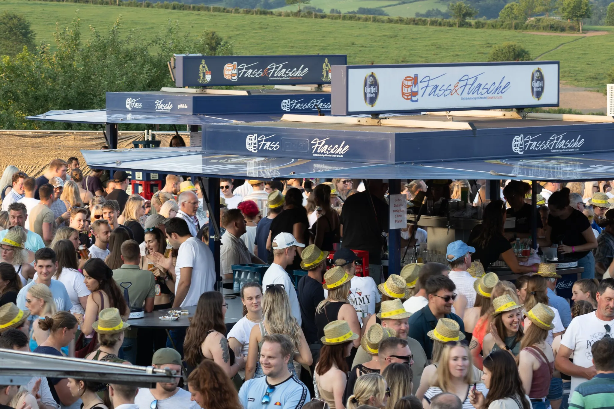 Besucherinnen und Besucher stehen dicht gedrängt an den Getränkeständen, entspannte Festivalstimmung im späten Nachmittagslicht.