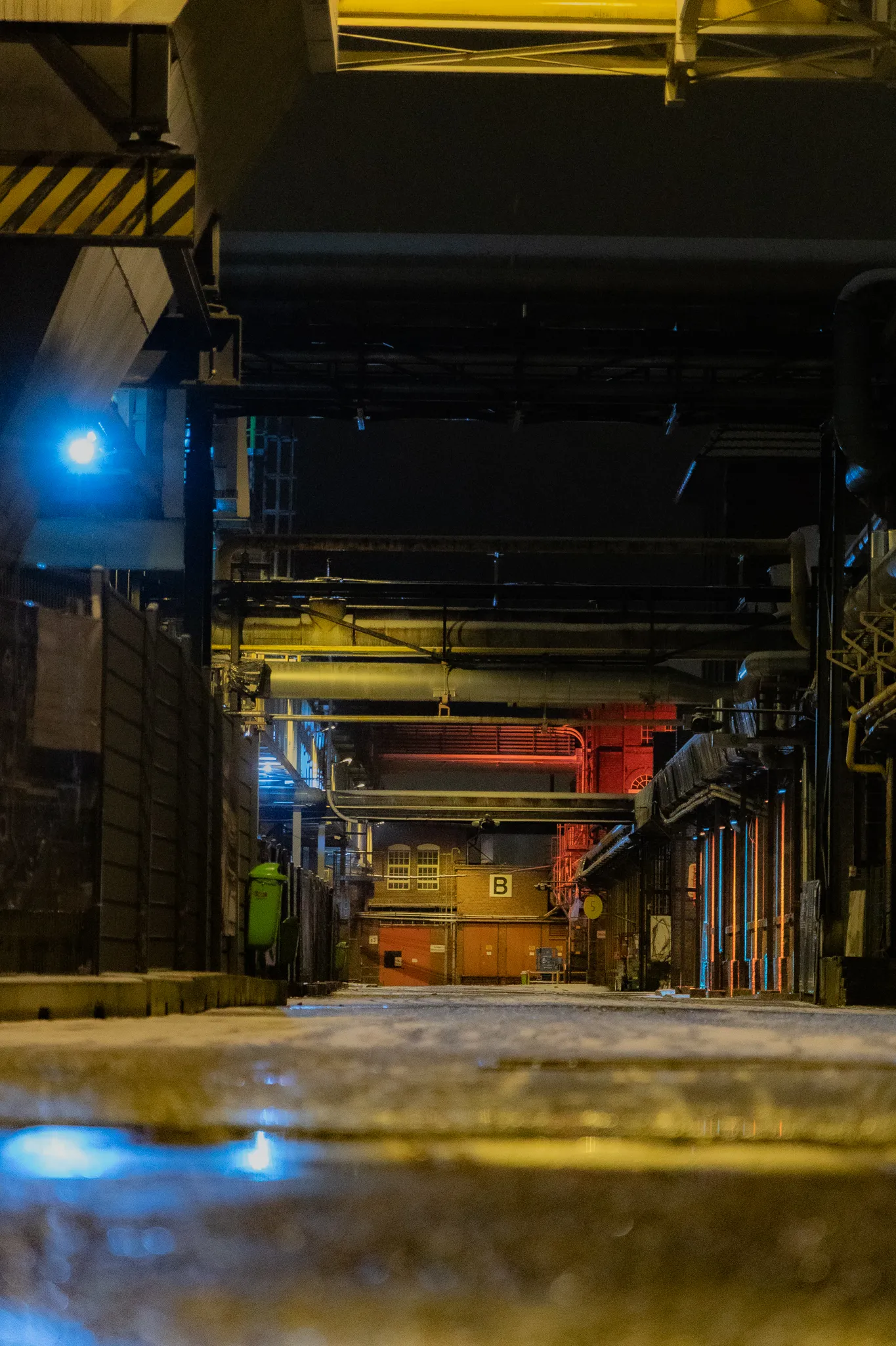 Blick eine schneebedeckte Werksgasse hinunter auf das rot illuminierte Zanders-Gebäude mit der Aufschrift „B“, im Vordergrund ein blauer Lichtreflex.