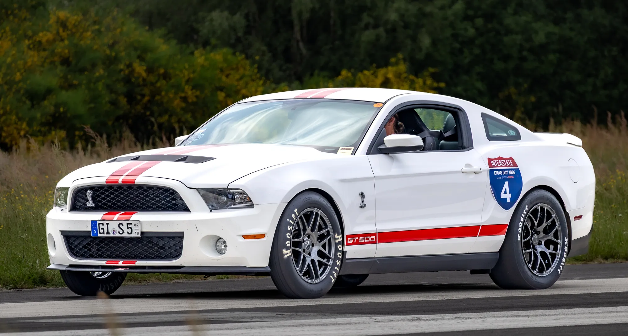 Ford Mustang mit orange-blauer WRAPWORKS-Rennfolierung, Startnummer 43 und Sponsorenaufklebern (Falken, Brembo, Recaro), auf der Startbahn fahrend.