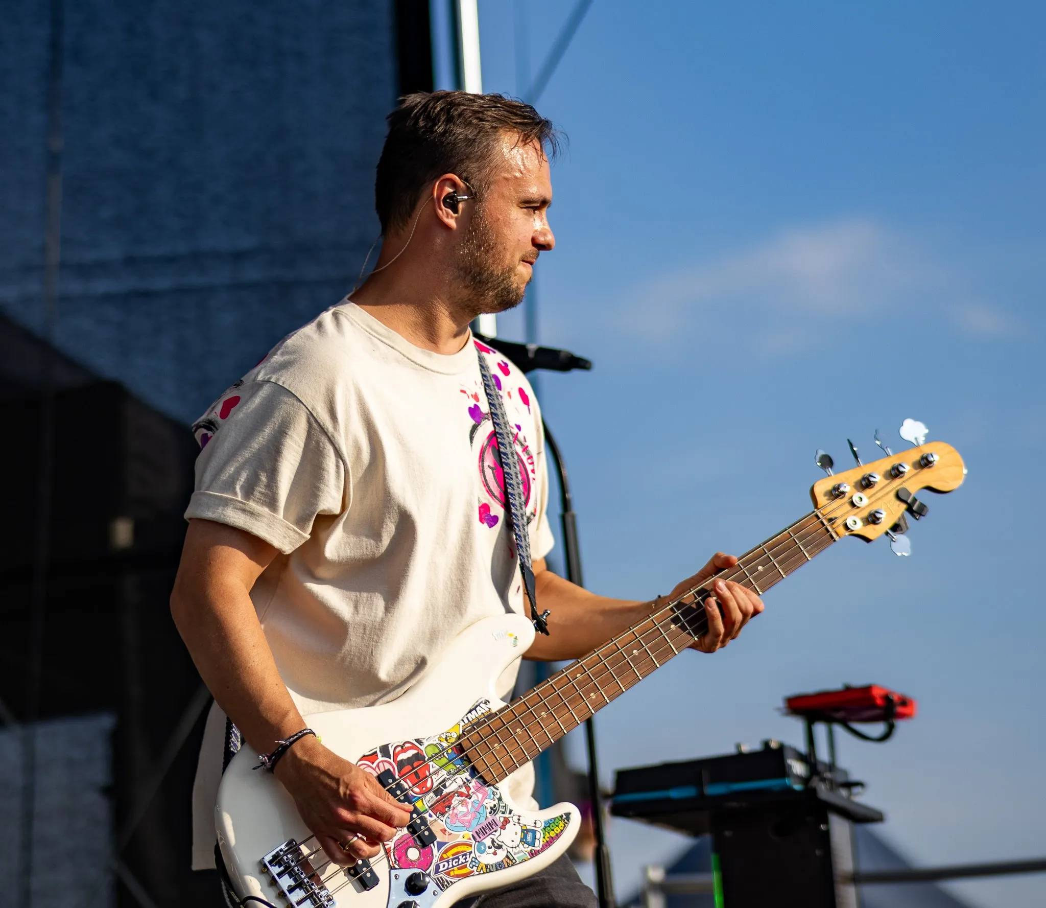 Bassist mit bunt beklebtem Bass blickt konzentriert auf sein Griffbrett, Tageslicht mit weichem Schattenwurf.