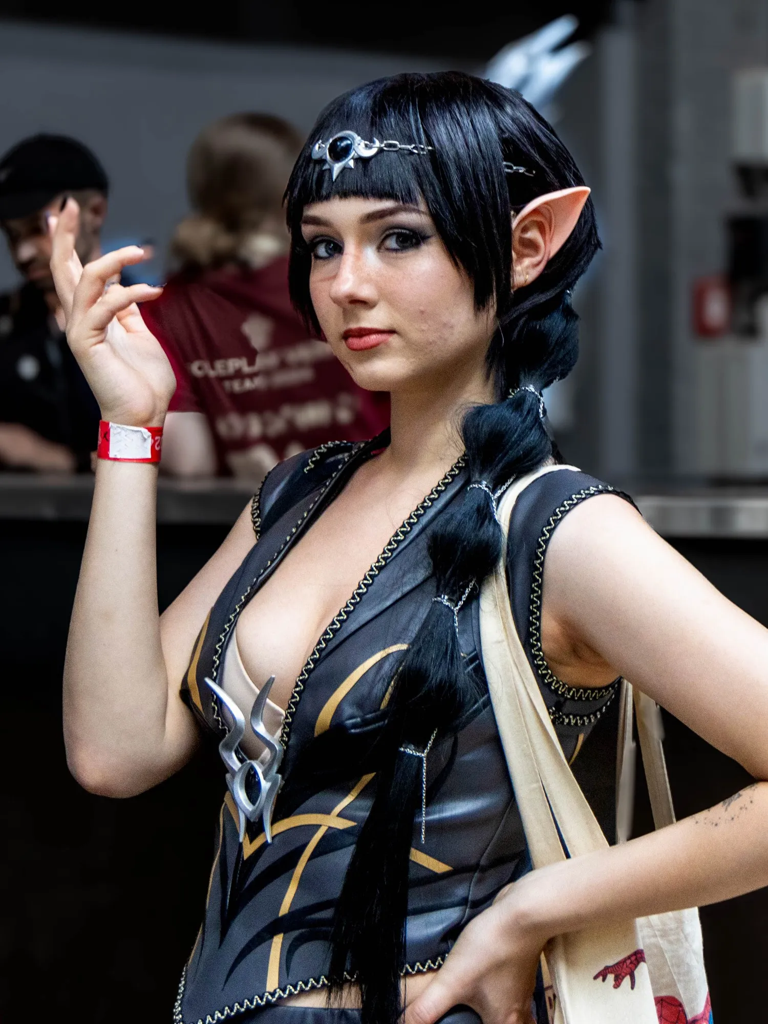 Cosplayerin in eng anliegendem schwarz-goldenem Outfit mit spitzen Ohren, erhobener Hand in selbstbewusster Pose auf einer Cosplay-Messe.